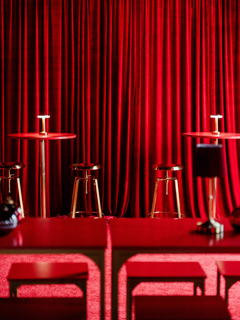 Wide view of the Santa Baby pop-up bar featuring red velvet walls, red high-top tables, and brass stools designed by Columbus event design studio Aisle & Co.