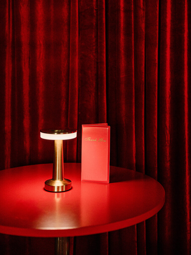 Holiday pop-up tabletop featuring a brass lamp and red thank-you folio inside the Santa Baby bar designed by Aisle & Co. at The Junto Hotel.