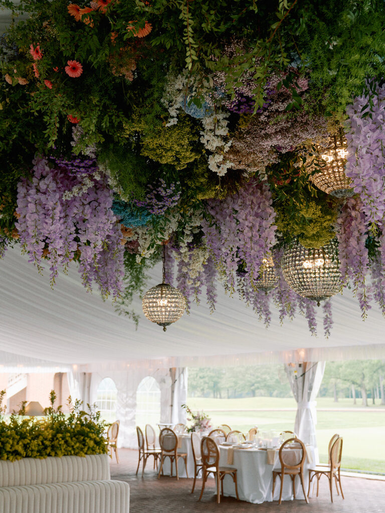 Tent reception with hanging floral ceiling and crystal chandeliers.