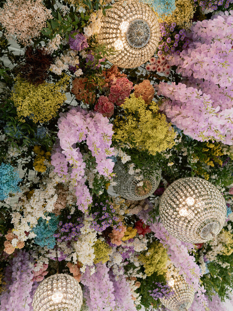 Tent reception with hanging floral ceiling and crystal chandeliers.